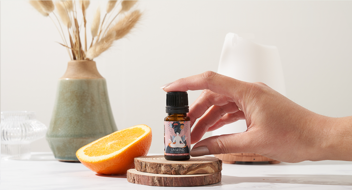 A bottle of unwind essential oil blends with an orange and decorative elements on a light background.