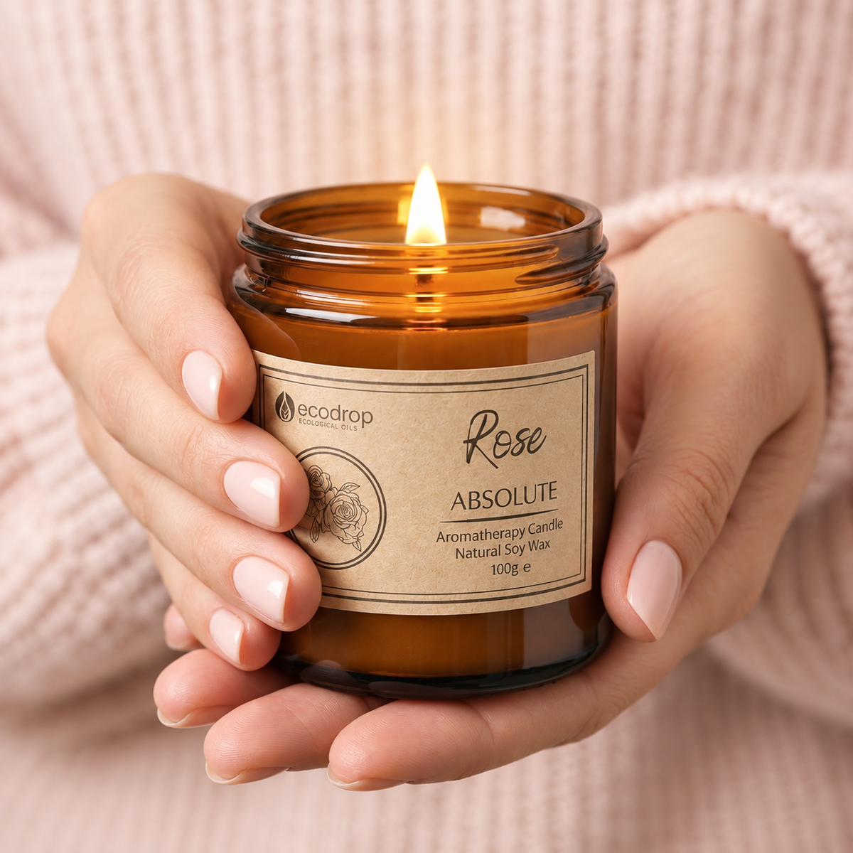 Hands holding an Ecodrop Rose Absolute aromatherapy candle in an amber glass jar