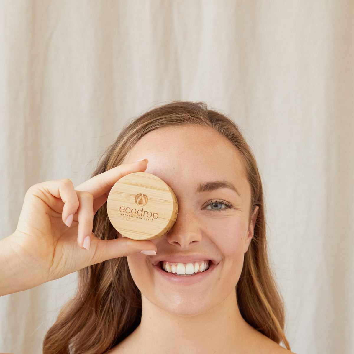 Smiling woman holding the bamboo lid of Ecodrop Comfort Cream