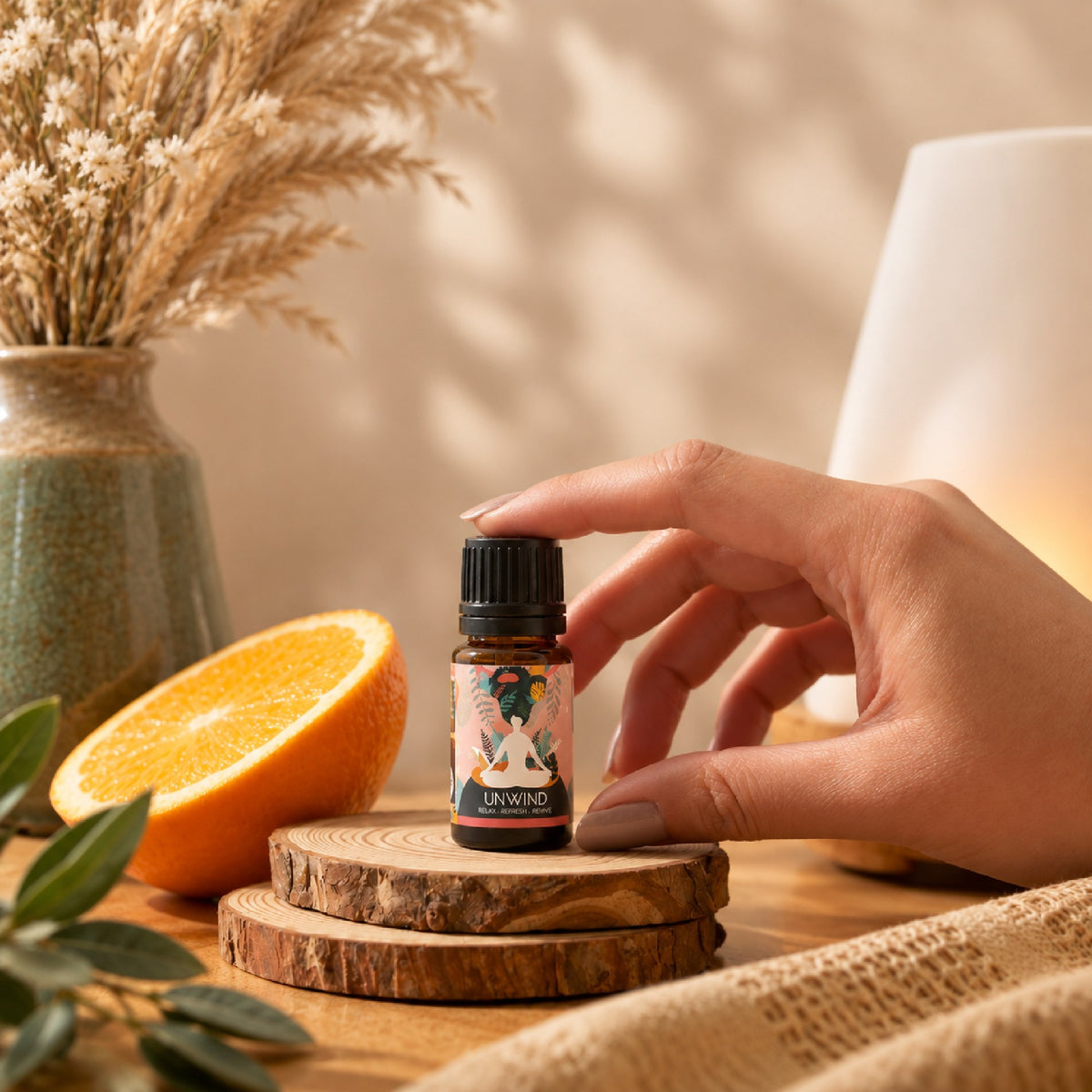 Hand placing the Unwind blend on a wooden slice beside a halved orange