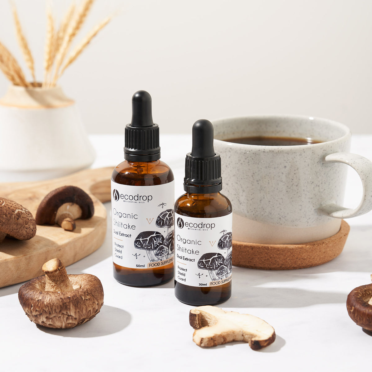 Ecodrop Organic Shiitake dual extract in 30ml and 50ml dropper bottles, beside fresh shiitake mushrooms and a cup of coffee