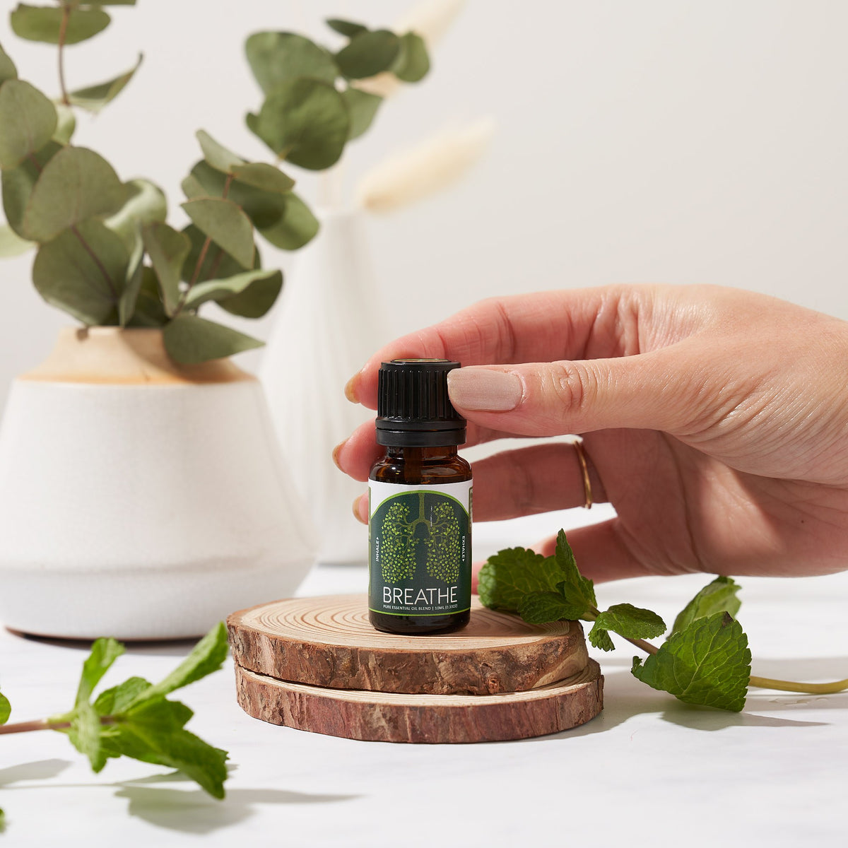 Breathe Easy blend bottle held on a wooden slice with fresh mint and eucalyptus