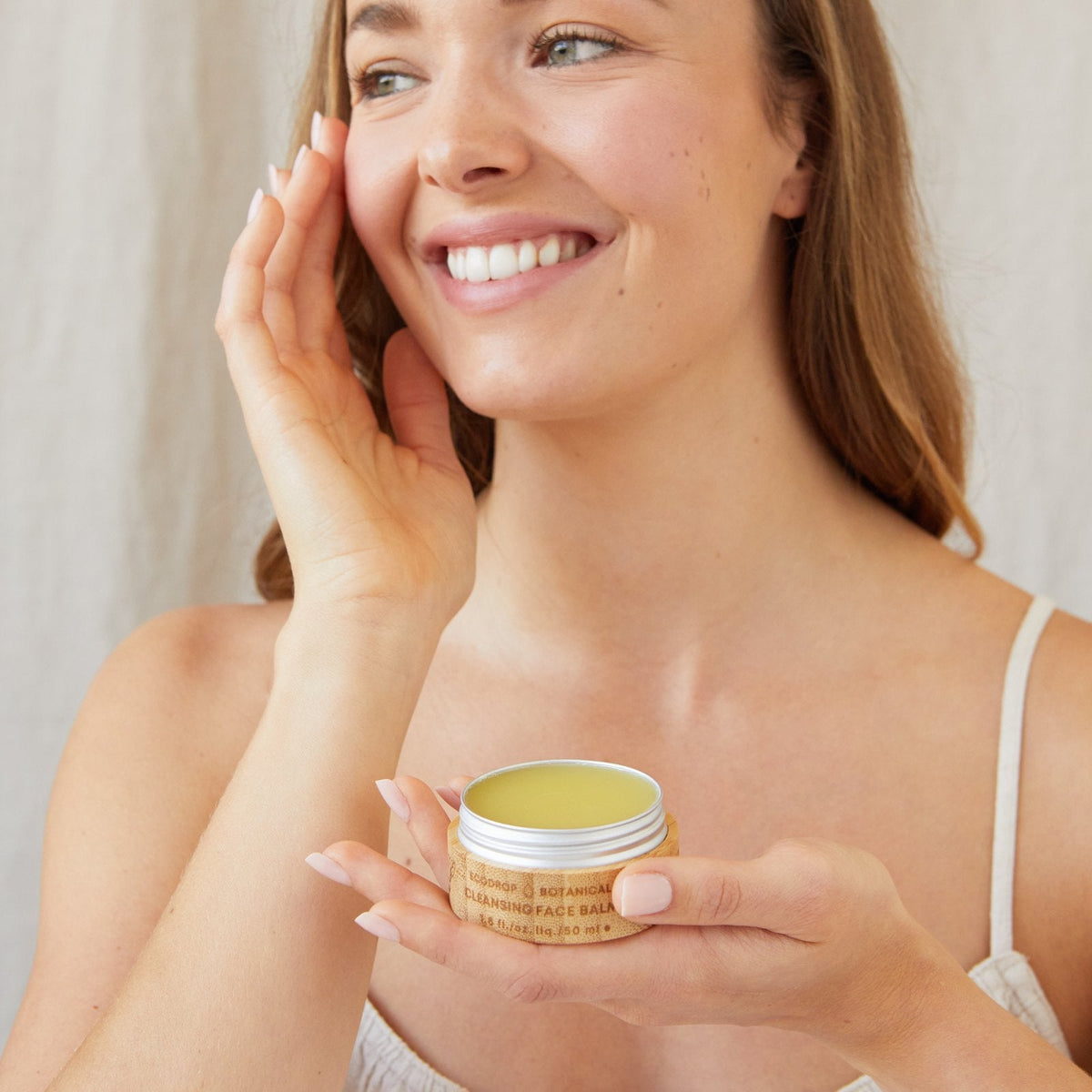 Woman holding an open tin of Ecodrop calendula cleansing balm for dry skin