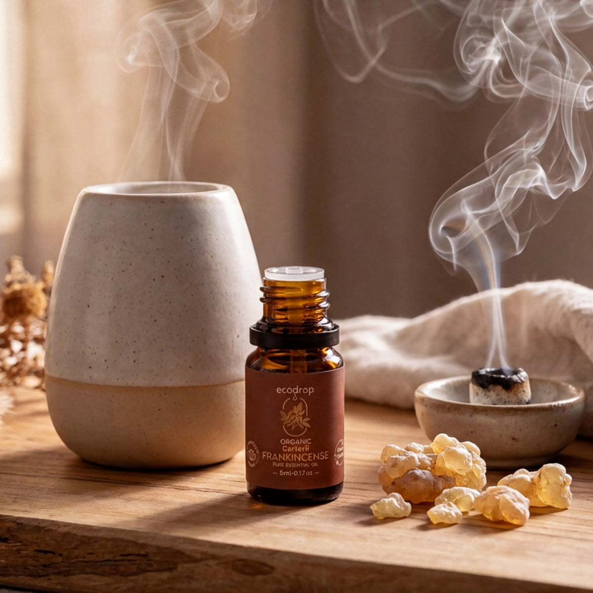 Frankincense Carterii essential oil beside a ceramic diffuser, burning resin and golden frankincense tears