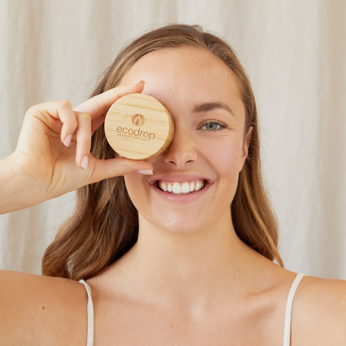 Woman smiling holding an Ecodrop natural skin care bamboo lid over her eye