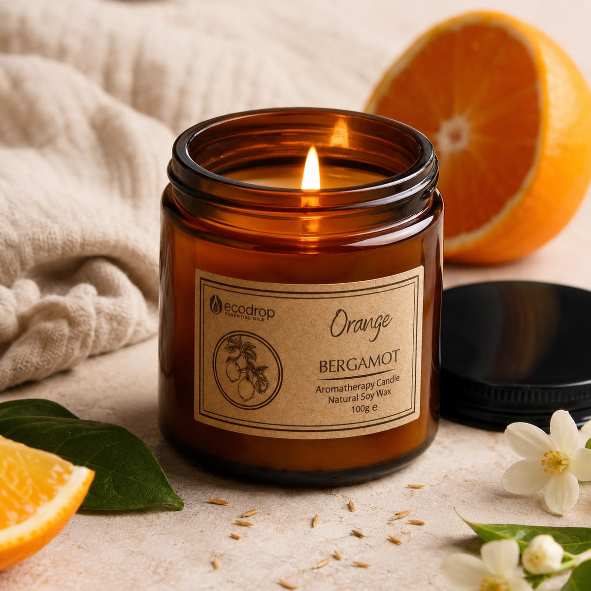 Lit Orange & Bergamot candle with a fresh halved orange, orange blossom and its black lid
