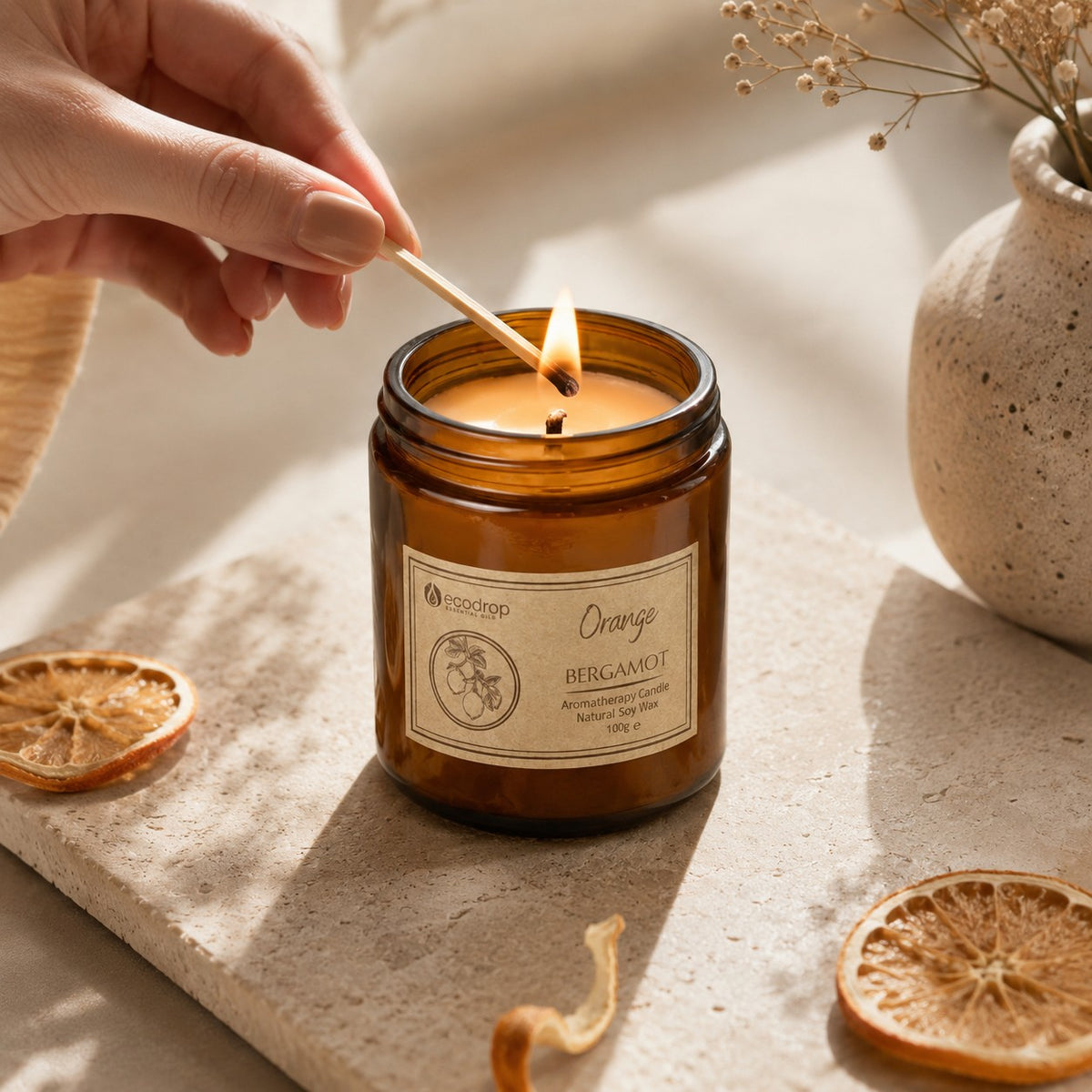Match lighting the cotton wick of the Orange & Bergamot soy candle, dried orange slices nearby