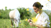 Woman using Ecodrop organic essential oil with a dropper in a flower field, horse grazing in the background