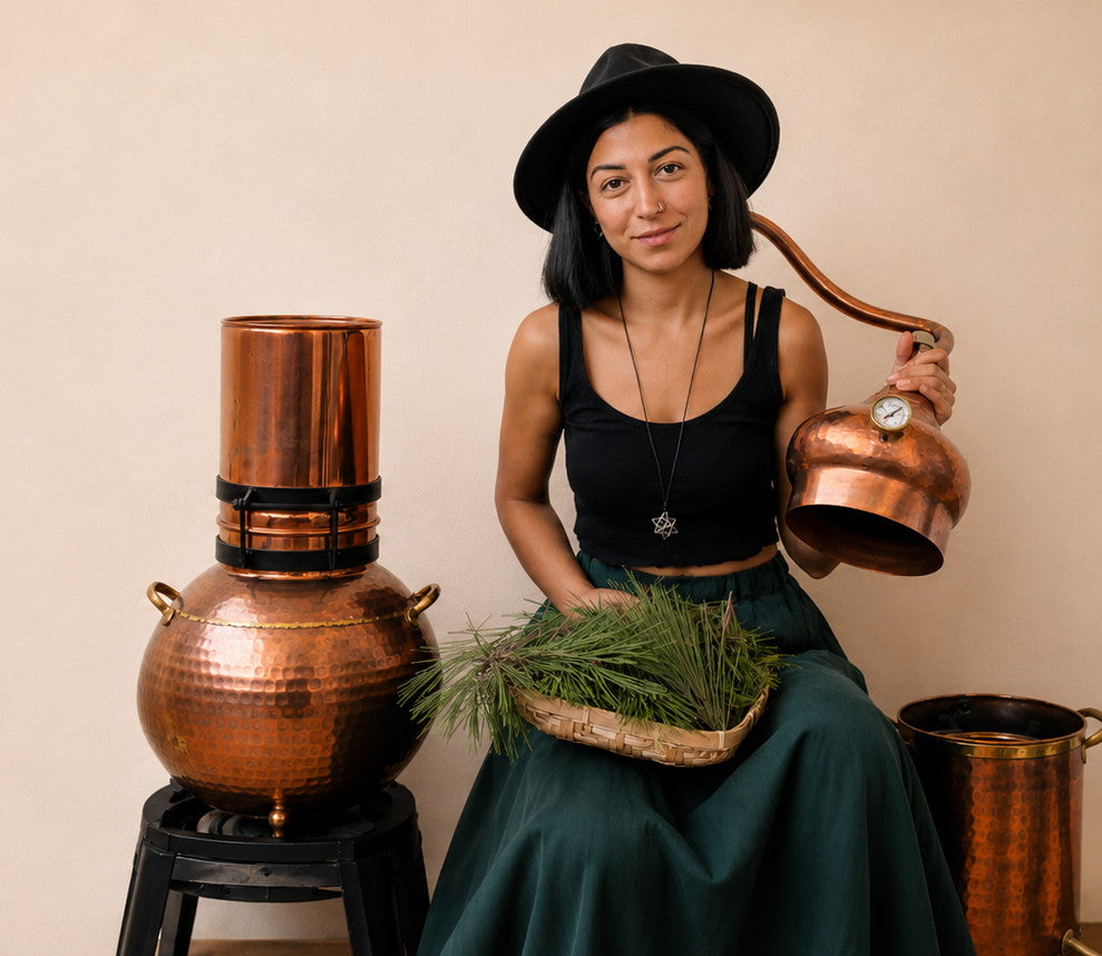 Rosa, co-founder of Ecodrop, beside a copper alembic still with pine and botanicals