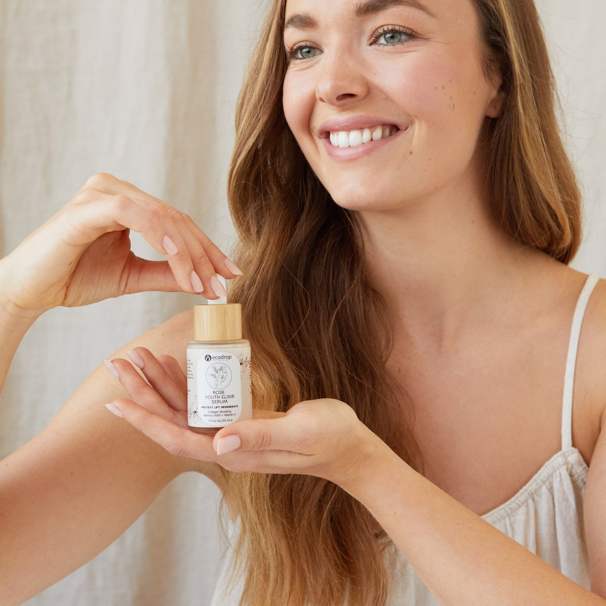 Woman smiling and holding Ecodrop Rose Youth Elixir peptide face serum