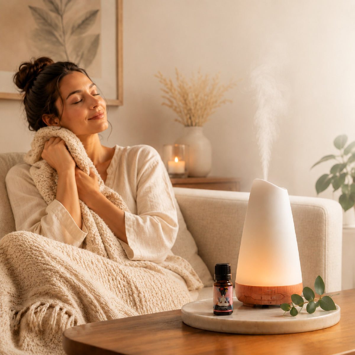 Woman wrapped in a blanket on the sofa beside a diffuser and Unwind blend