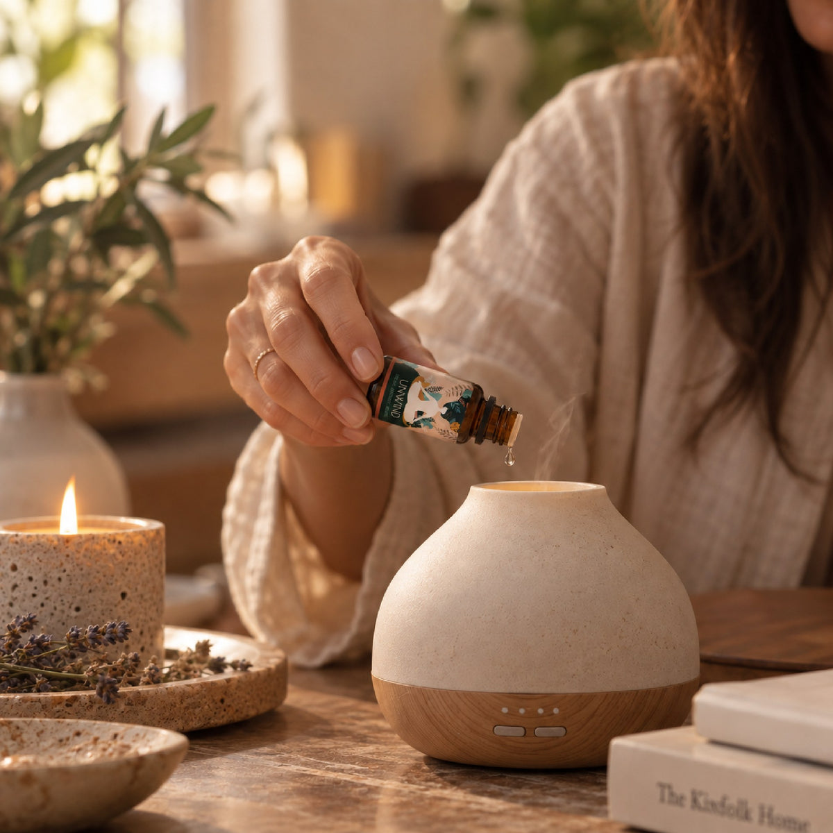 Drops of Unwind blend going into a stone diffuser beside a candle