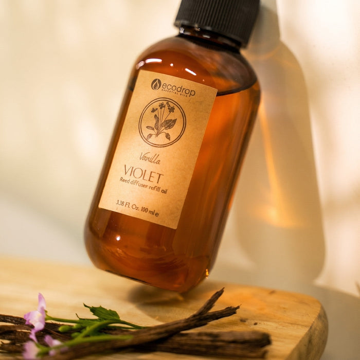 Vanilla Violet reed diffuser refill bottle backlit with violet flowers and vanilla pods